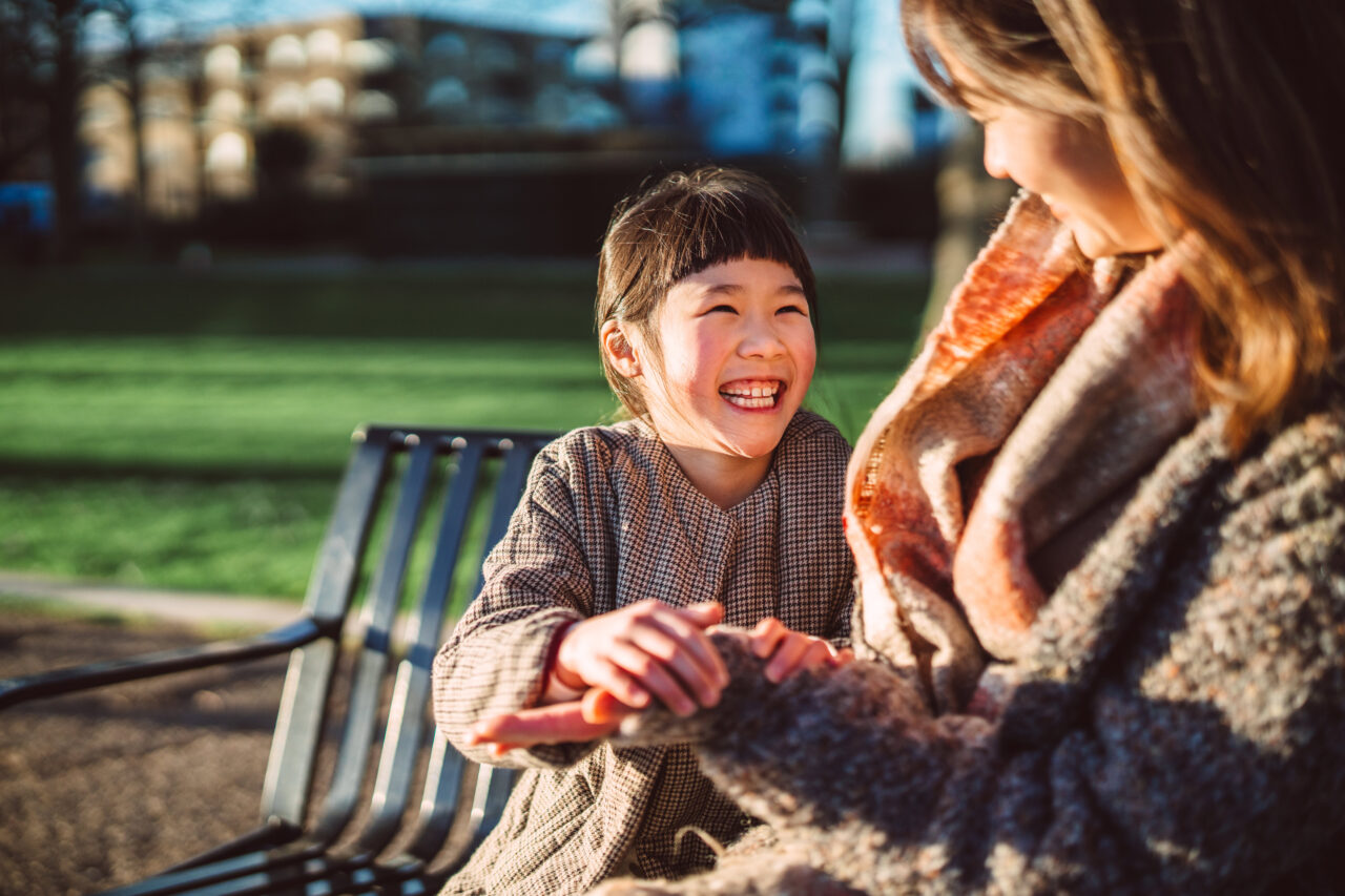 Joyful moment between mother and daughter on a sunny park bench